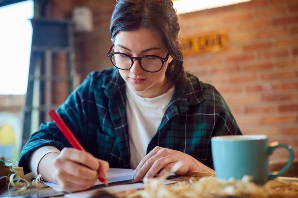 young female carpenter drawing and measuring woodw